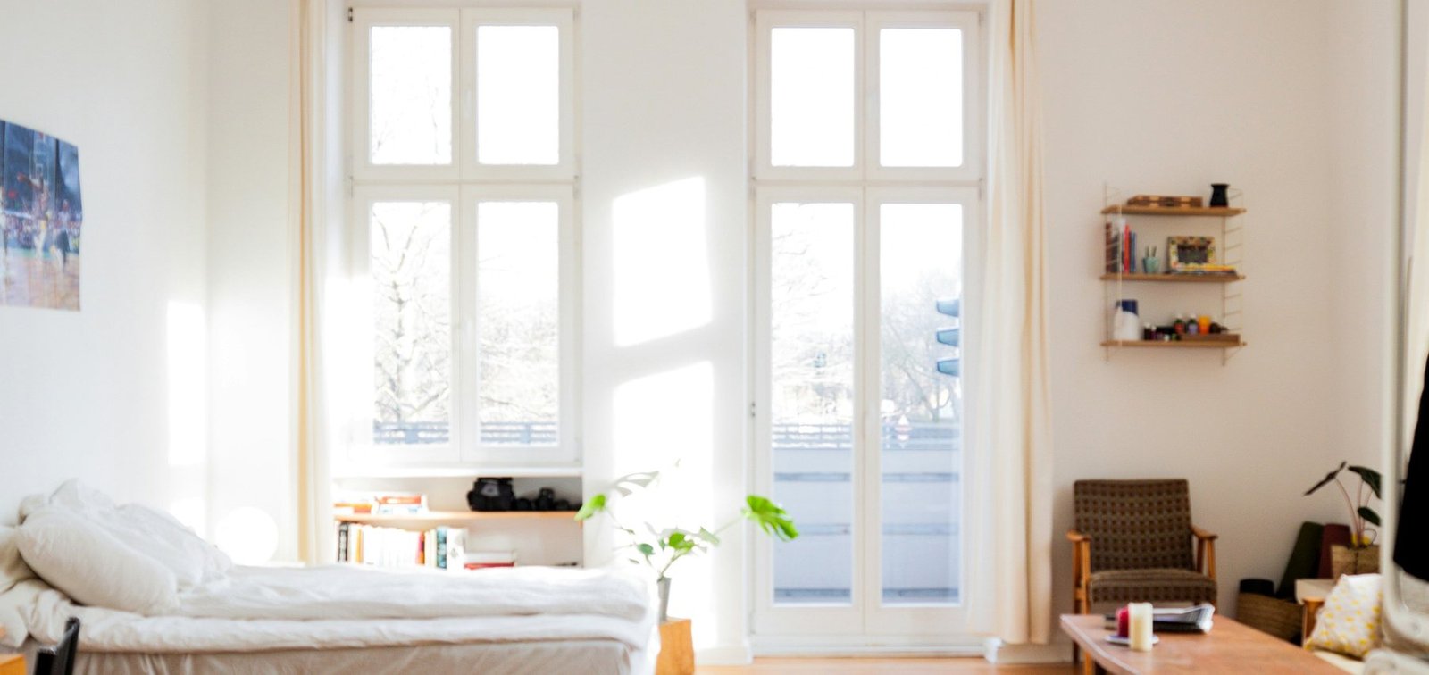 Professionally photographed bright compact room with a bed, shelving and tall windows, representing the everyday housing access RentHub Ghana works to improve.