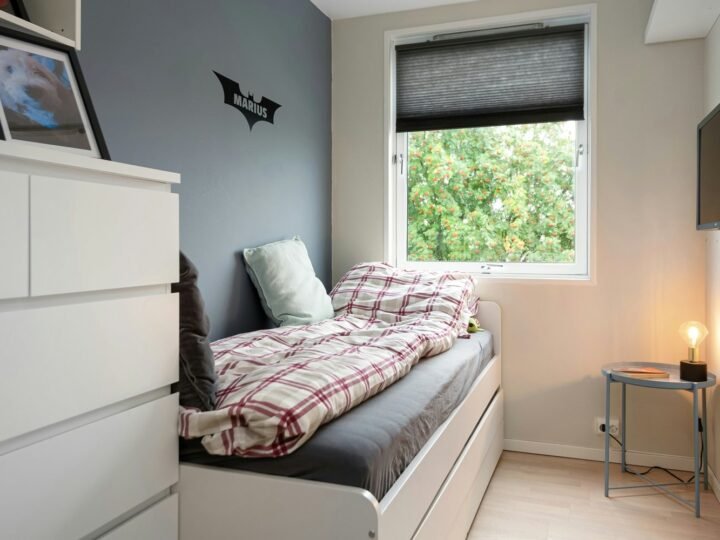 Professional photograph of a compact student bedroom with a single bed, storage drawers, wall-mounted screen and window; representative demo image for the Kwadaso student apartment Gallery image 1 of 5 for Affordable Student Apartment in Kwadaso.