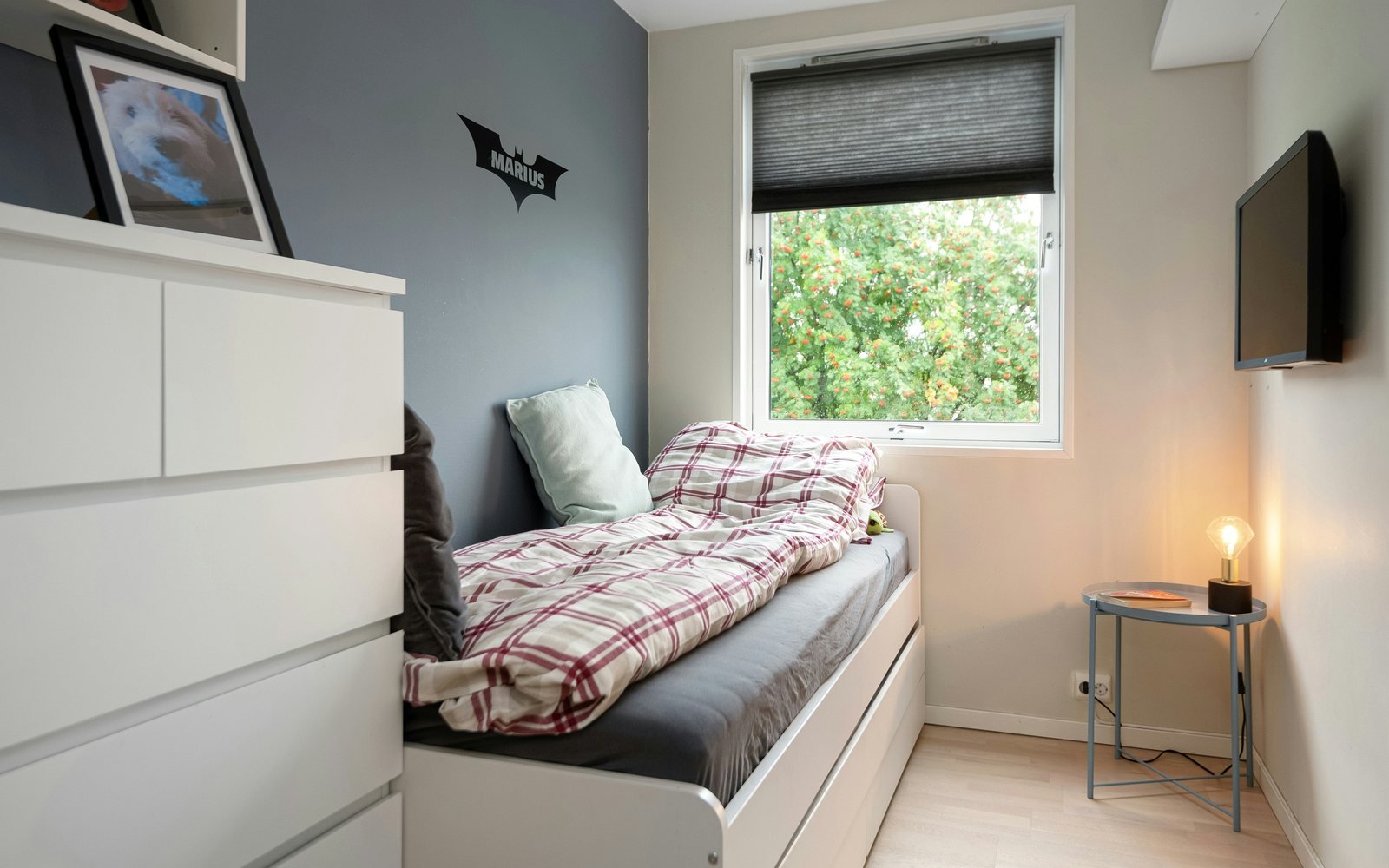 Professional photograph of a compact student bedroom with a single bed, storage drawers, wall-mounted screen and window; representative demo image for the Kwadaso student apartment Gallery image 1 of 5 for Affordable Student Apartment in Kwadaso.